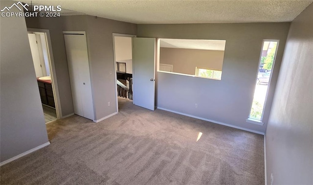 unfurnished bedroom featuring carpet floors, a textured ceiling, connected bathroom, and multiple windows