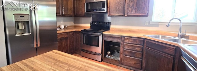 kitchen with dark brown cabinetry, butcher block countertops, stainless steel appliances, and sink