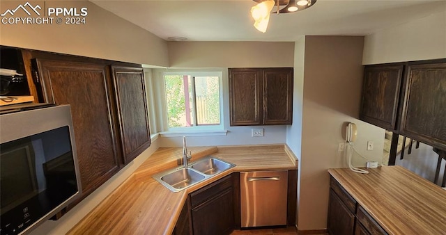 kitchen featuring appliances with stainless steel finishes, dark brown cabinetry, sink, and wood counters