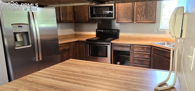 kitchen with dark brown cabinetry, stainless steel appliances, and wooden counters