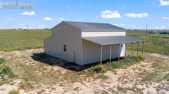 view of outdoor structure with a lawn, a rural view, and a carport