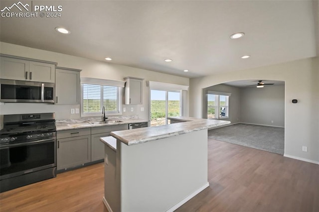 kitchen with light stone counters, stainless steel appliances, sink, wood-type flooring, and ceiling fan