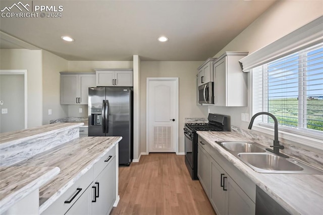 kitchen featuring light wood-type flooring, light stone counters, sink, appliances with stainless steel finishes, and gray cabinetry