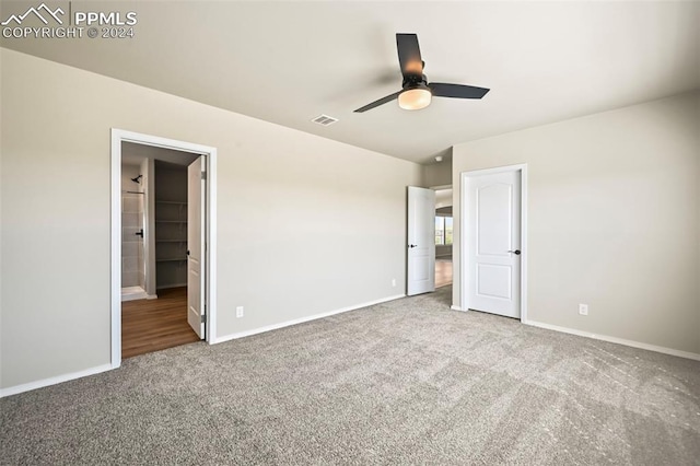 unfurnished bedroom with a walk in closet, a closet, ensuite bathroom, carpet flooring, and ceiling fan