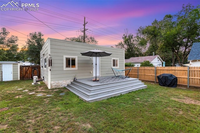 back house at dusk featuring a storage unit and a lawn