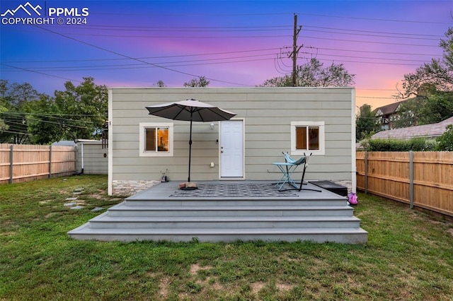 back house at dusk featuring a lawn and a wooden deck