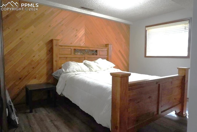 bedroom with a textured ceiling, wooden walls, and hardwood / wood-style floors