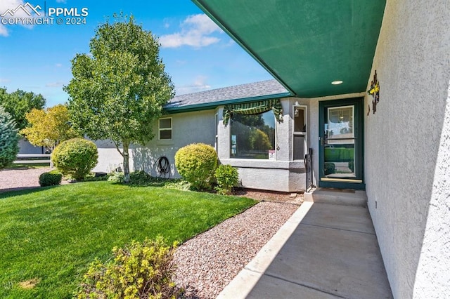 entrance to property featuring roof with shingles, a yard, and stucco siding