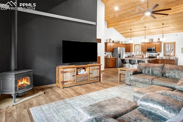 living room with a wood stove, wood ceiling, high vaulted ceiling, ceiling fan, and light wood-type flooring