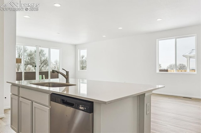 kitchen featuring a sink, light countertops, stainless steel dishwasher, light wood finished floors, and a center island with sink