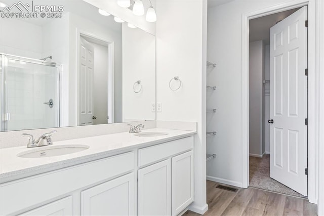 full bath featuring double vanity, a sink, a shower stall, and wood finished floors