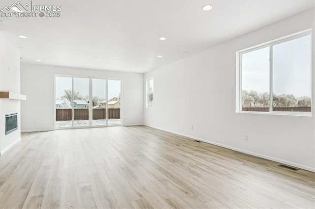 unfurnished living room with visible vents, baseboards, a glass covered fireplace, light wood-type flooring, and recessed lighting