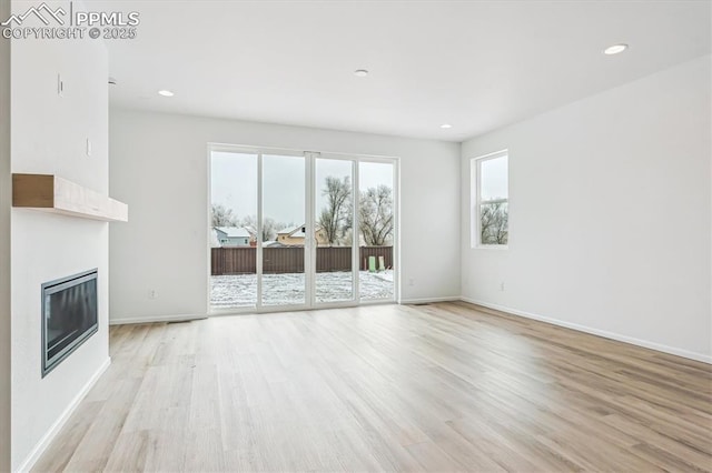 unfurnished living room with recessed lighting, light wood-style flooring, and a glass covered fireplace