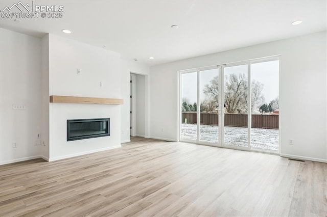 unfurnished living room with baseboards, a glass covered fireplace, wood finished floors, and recessed lighting