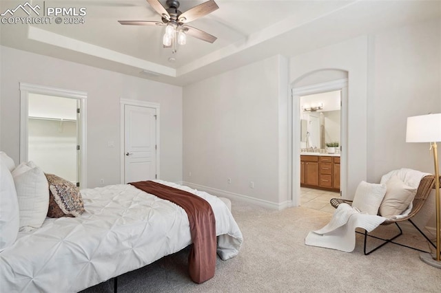 bedroom featuring connected bathroom, a raised ceiling, light carpet, and ceiling fan