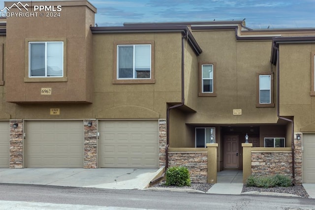 view of property with an attached garage, stone siding, driveway, and stucco siding