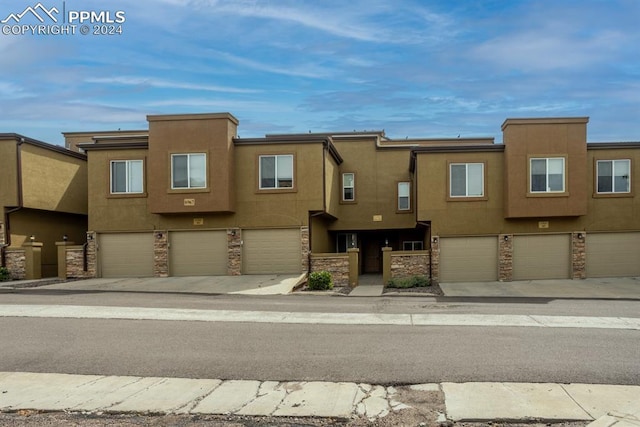 townhome / multi-family property with a garage, stone siding, and stucco siding