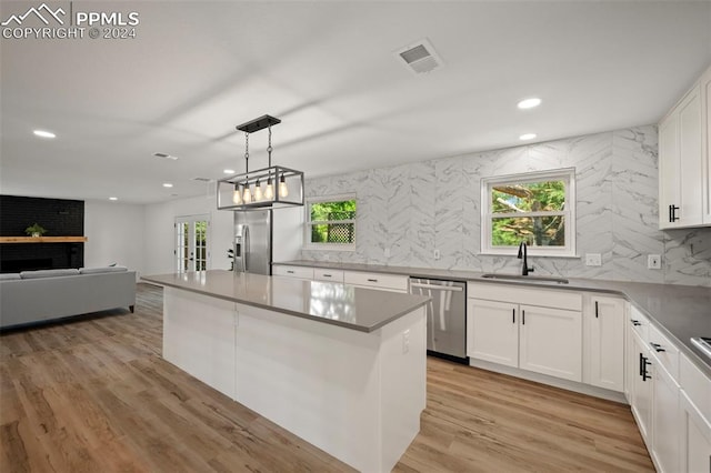 kitchen with pendant lighting, appliances with stainless steel finishes, white cabinetry, a sink, and a kitchen island