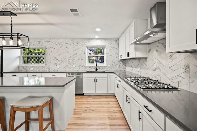 kitchen featuring a breakfast bar, stainless steel appliances, dark countertops, a sink, and wall chimney exhaust hood