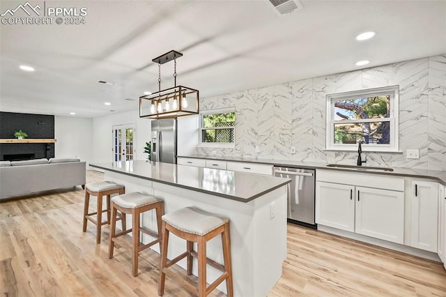 kitchen with stainless steel appliances, a sink, white cabinetry, dark countertops, and decorative light fixtures