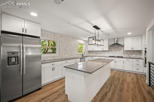 kitchen with appliances with stainless steel finishes, a center island, white cabinetry, and wall chimney exhaust hood