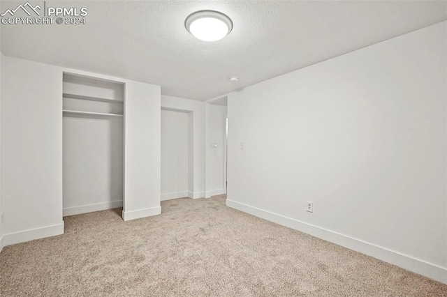 unfurnished bedroom with light carpet, a closet, baseboards, and a textured ceiling