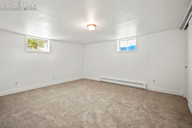 basement featuring a baseboard heating unit, a wealth of natural light, carpet flooring, and a textured ceiling