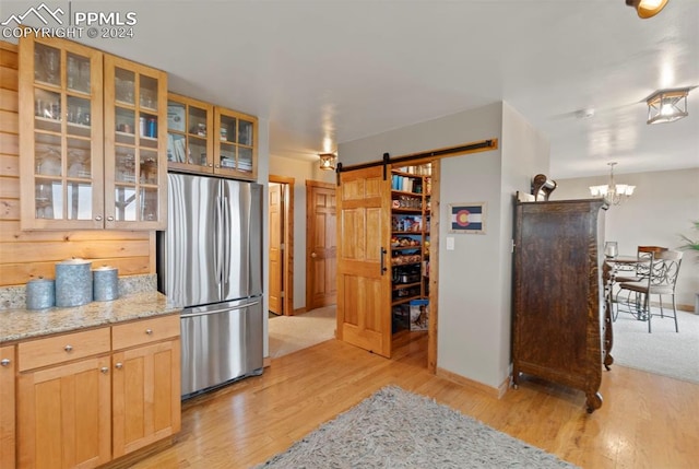 kitchen featuring stainless steel fridge, light brown cabinetry, a notable chandelier, a barn door, and light wood-type flooring