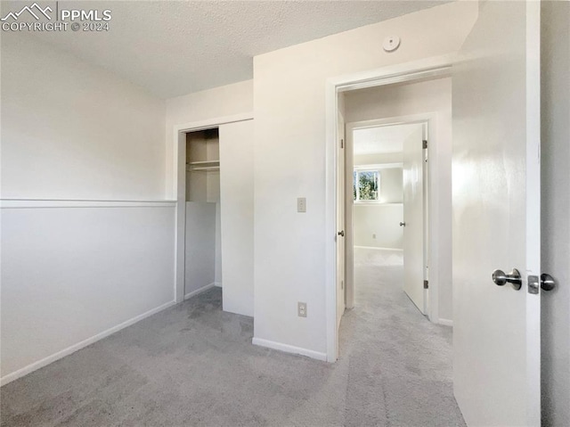 unfurnished bedroom with a textured ceiling, a closet, and light carpet