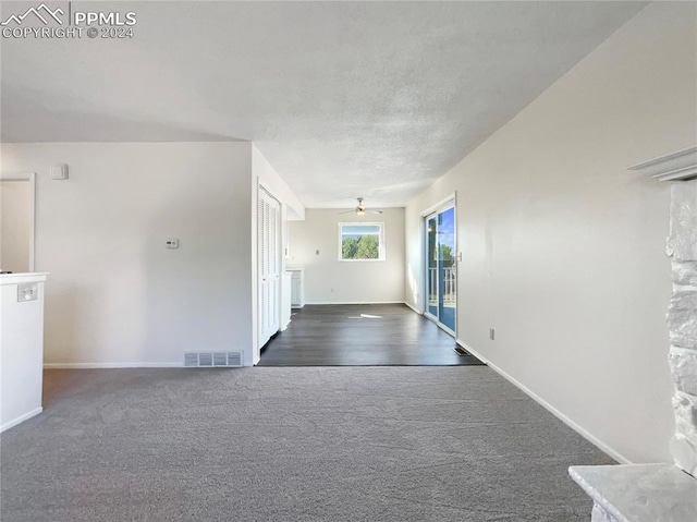 interior space with a textured ceiling, dark colored carpet, and ceiling fan