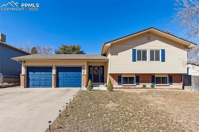 tri-level home featuring a garage, fence, driveway, and brick siding