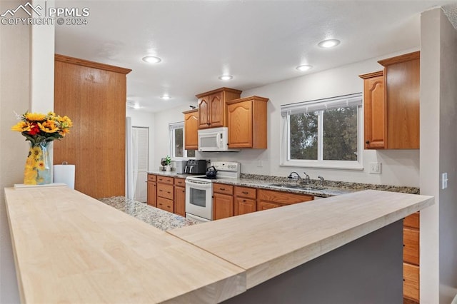 kitchen featuring recessed lighting, white appliances, a peninsula, brown cabinets, and a sink