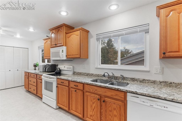 kitchen with a sink, a wealth of natural light, white appliances, and light stone counters