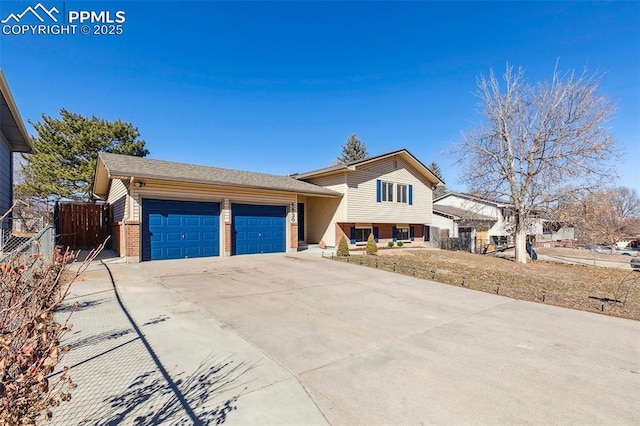 split level home with an attached garage, concrete driveway, fence, and brick siding