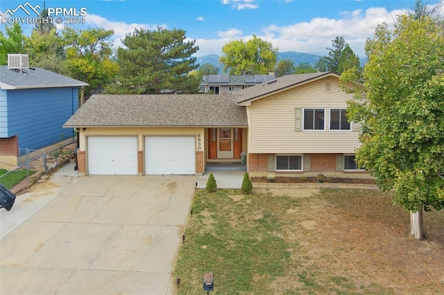 tri-level home featuring a mountain view, fence, brick siding, an attached garage, and driveway