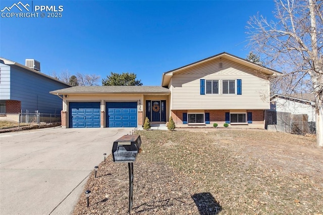 tri-level home with a garage, brick siding, fence, and concrete driveway
