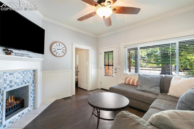 living room with ornamental molding, ceiling fan, a tiled fireplace, and hardwood / wood-style floors