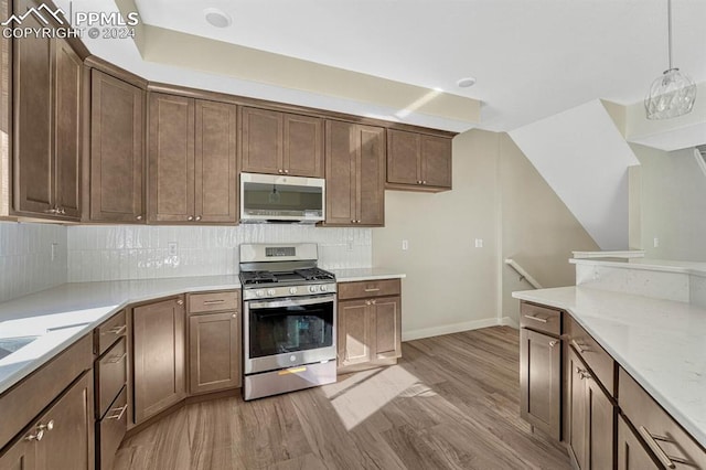 kitchen featuring light wood-style flooring, stainless steel appliances, baseboards, tasteful backsplash, and decorative light fixtures