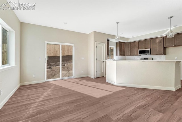 kitchen featuring hanging light fixtures, light wood-style floors, stainless steel microwave, and dark brown cabinets