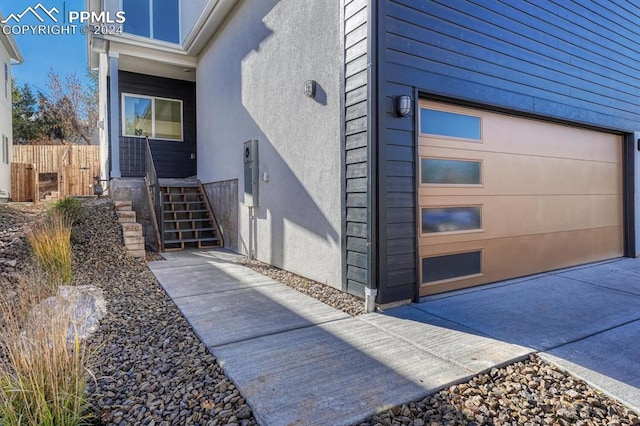 doorway to property with a garage, fence, and stucco siding