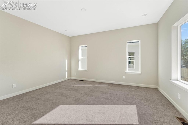 carpeted empty room featuring baseboards, visible vents, and a wealth of natural light