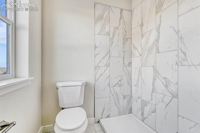 bathroom with a tile shower, toilet, and baseboards