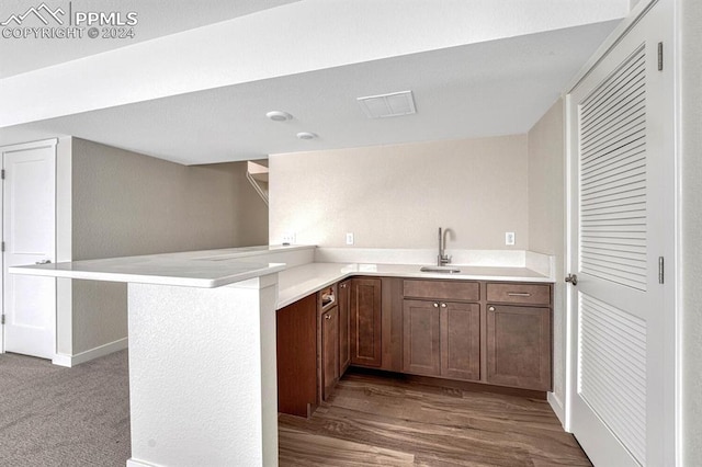 kitchen with a peninsula, light countertops, a sink, and wood finished floors