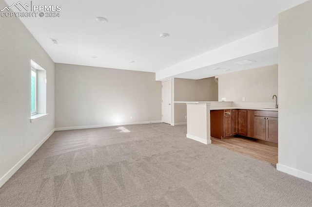 unfurnished living room featuring light colored carpet, a sink, visible vents, and baseboards