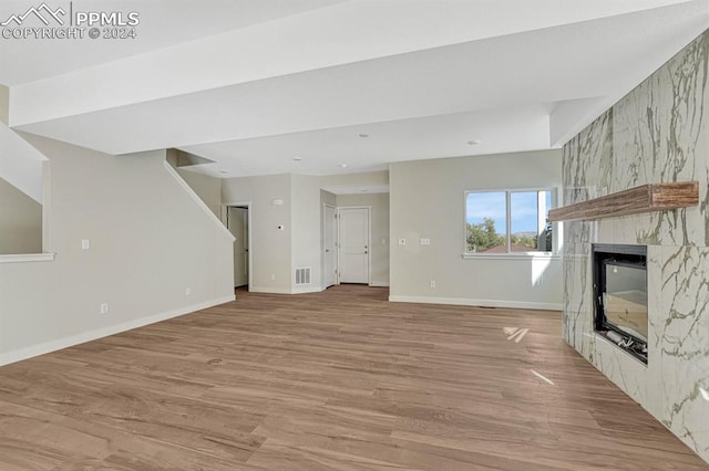 unfurnished living room with visible vents, light wood-type flooring, a high end fireplace, and baseboards