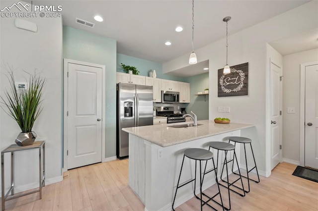 kitchen featuring a kitchen breakfast bar, decorative light fixtures, light hardwood / wood-style flooring, appliances with stainless steel finishes, and white cabinetry