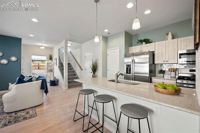 kitchen with appliances with stainless steel finishes, hanging light fixtures, sink, light stone counters, and light wood-type flooring