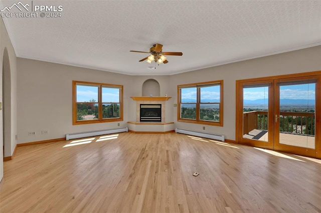 unfurnished living room featuring light wood-type flooring, a fireplace, a wealth of natural light, ceiling fan, and a baseboard heating unit