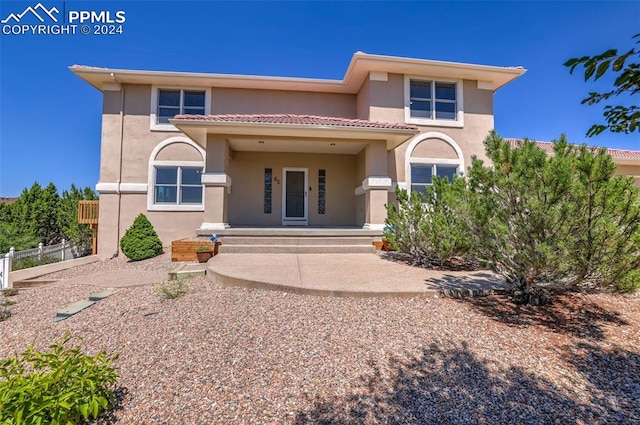 view of front of home featuring stucco siding, covered porch, a tiled roof, and fence