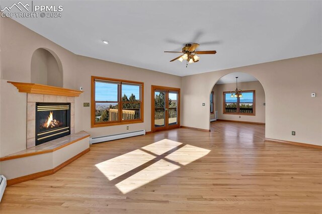 unfurnished living room featuring baseboard heating, light wood-type flooring, a tile fireplace, and ceiling fan